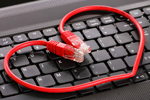 Red data cable wrapped in the shape of a heart, on keyboard, symbolizing internet dating